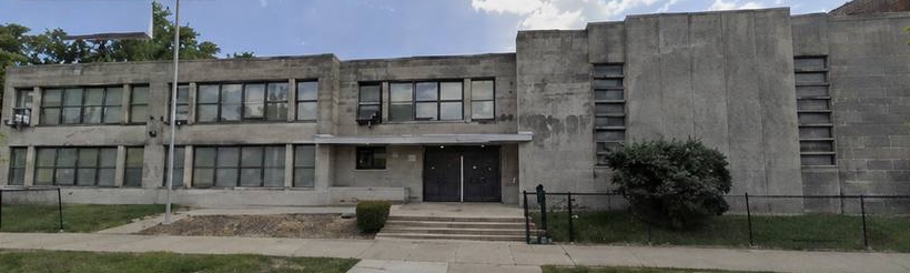 The former Marva Collins School today: a weathered grey concrete building with boarded windows, stained facade, bare ground, and a chain-link fence.