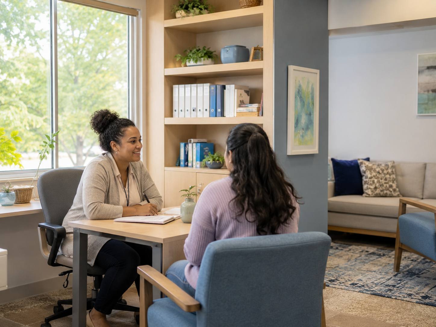 Concept image of a family support worker sitting and talking with a parent in a bright, softly furnished room.
