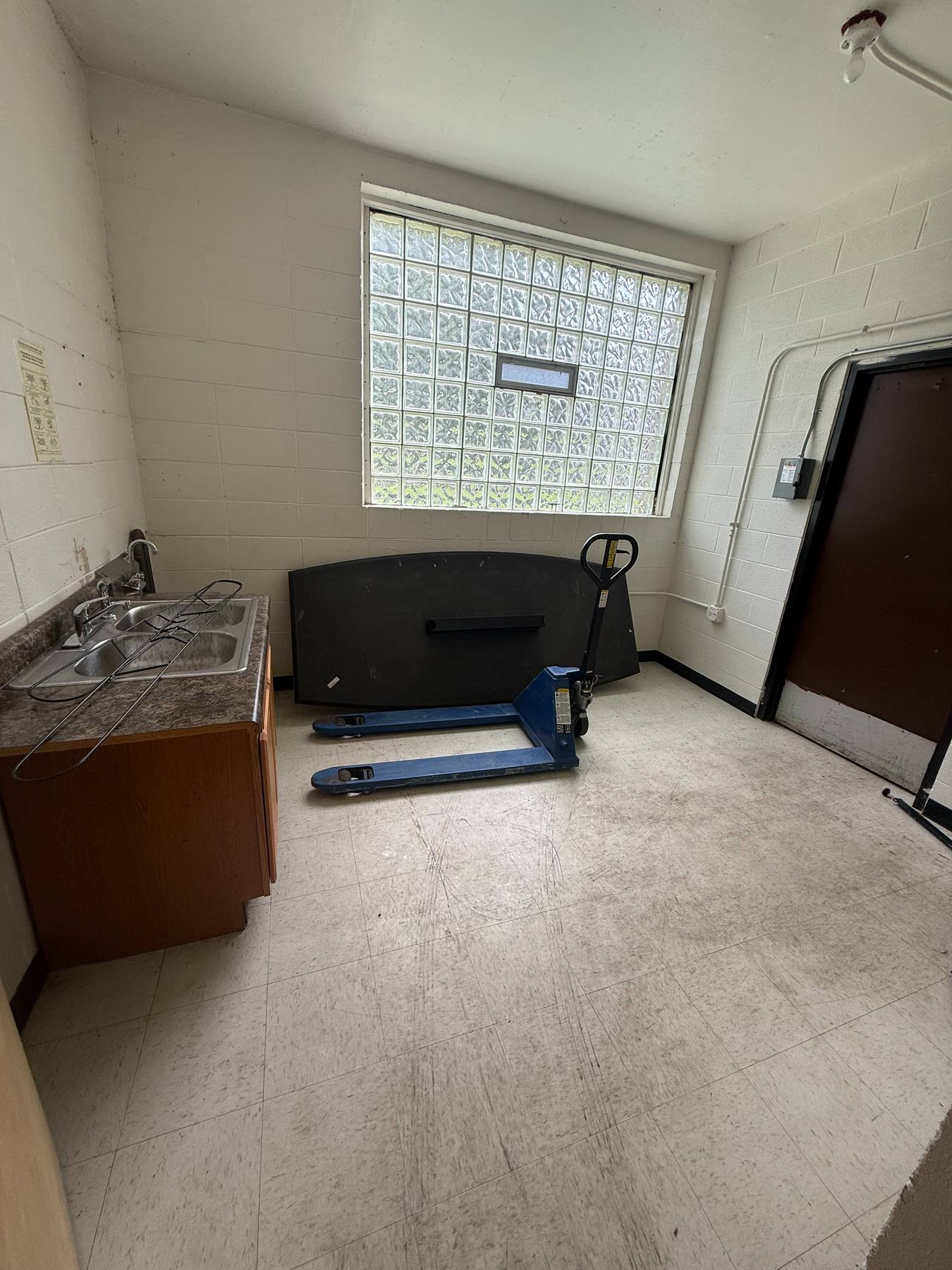 A stripped service room with a single old sink and a glass-block window.